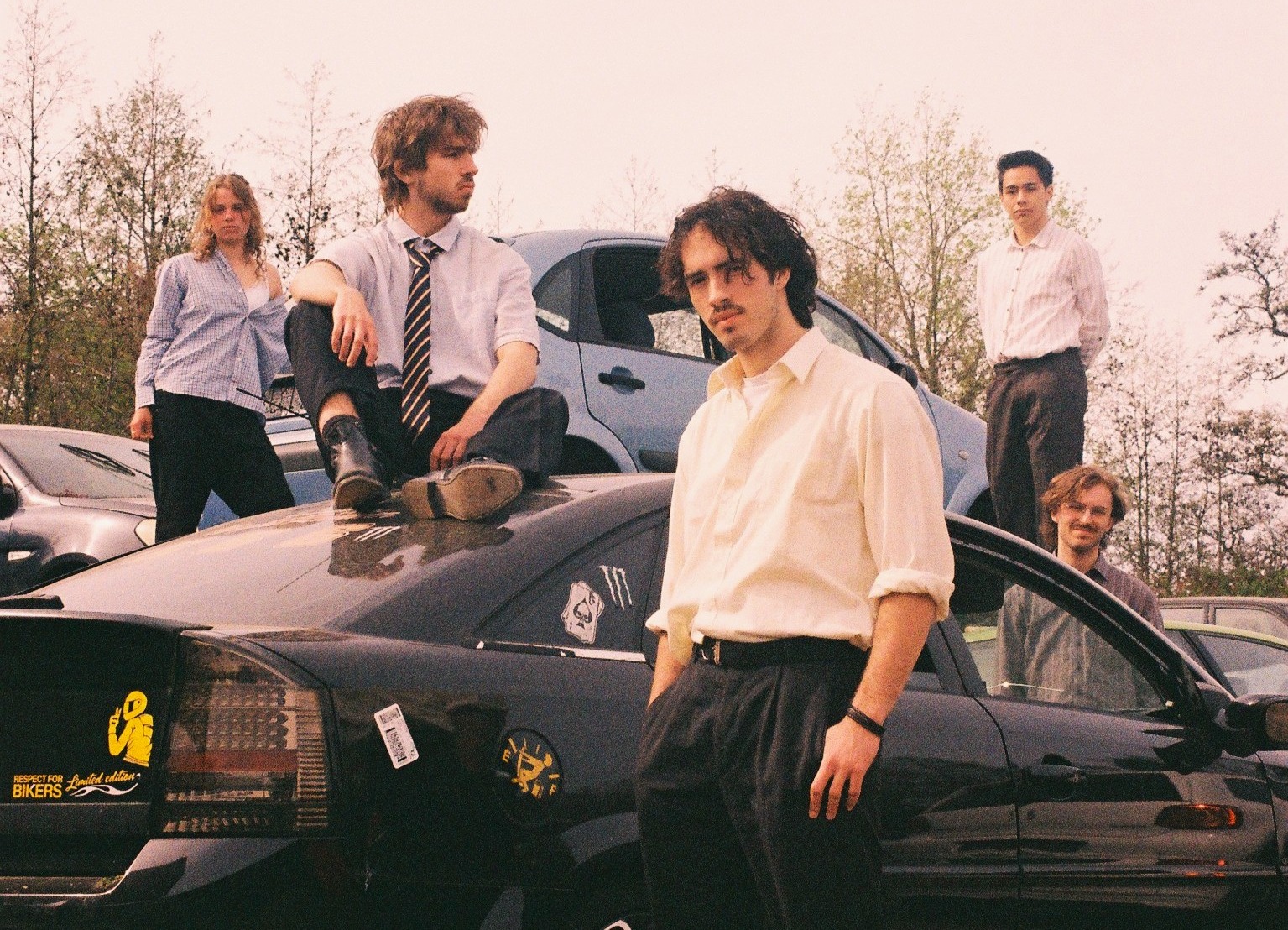 Dit is een foto van de band See Sharp, er staan vier personen rondom een auto geposeerd.